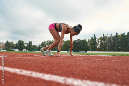 Side view of professional young female runner in sportswear starting race on track field at stadium
