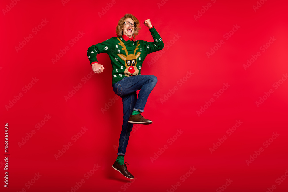 Photo of funny lucky young guy dressed print pullover smiling jumping rising arms empty space isolated red color background Photo of funny lucky young guy dressed print pullover smiling jumping rising arms empty space isolated red color background