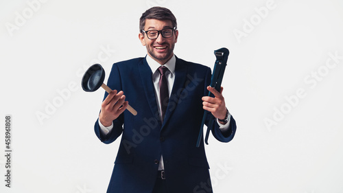 Positive businessman holding plunger and pipe wrench isolated on white