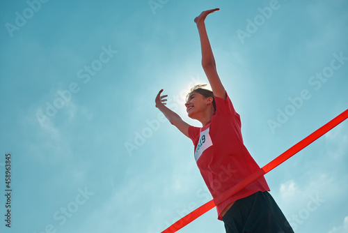 Low angle view of cheerful young female runner with arms raised reaching the finish line at track field during marathon outdoors