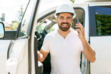 Man engineer builder wearing a white hard hat, shirt in front of his pickup using cellphone
