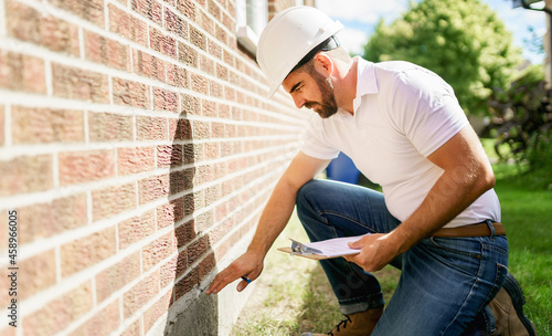 man with a white hard hat holding a clipboard, inspect house