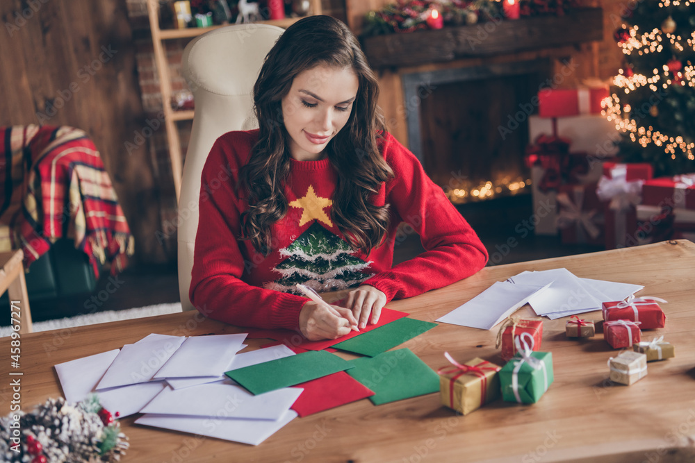 Photo of sweet pretty young woman dressed print pullover smiling writing christmas wishes indoors room home house