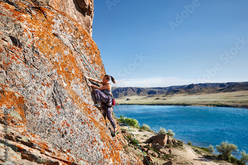 Young woman climb the rock near blue river