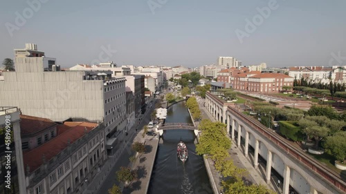 Aerial descending shot of moliceiro boat cruising on water canal under pedestrian bridge.