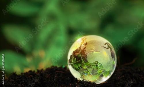 Crystal Earth On Soil In Forest With Sunlight - The Environment - Earth Day Concept. glass globe on ground and green nature blur background earth day concept.