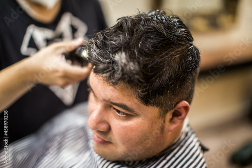 Male professional barber doing hair styling to handsome guy