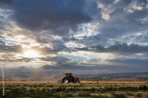 Dramatic sunset over a tractor working on the harvest