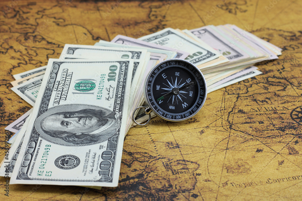 Classic navigation compass on background of old world map and american dollars as symbol of tourism with compass, travel with compass and outdoor activities with compass Classic navigation compass on background of old world map and american dollars as symbol of tourism with compass, travel with compass and outdoor activities with compass