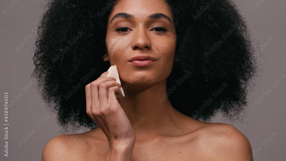 african american woman applying makeup foundation with sponge isolated on grey african american woman applying makeup foundation with sponge isolated on grey