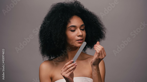 brunette african american woman using nail file isolated on grey photo
