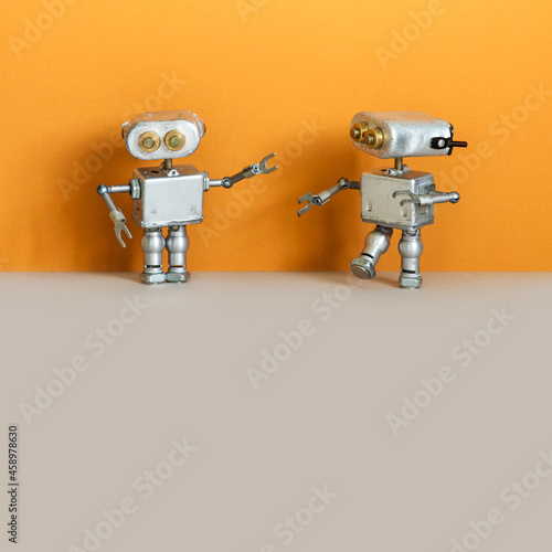 Two toy metal silver robots bots on an orange gray background. copy space for text