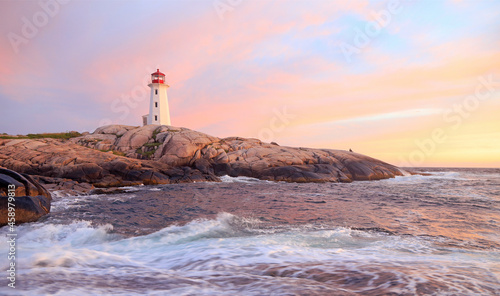 Peggy’s Cove Lighthouse illuminated at sunset with dramatic purple sky and waves, Nova Scotia, Canada
