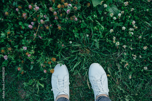 the legs of girl in a white shoes are standing in the tall green grass
