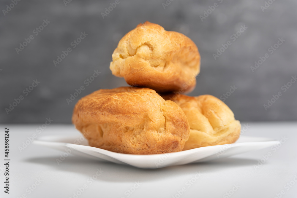 Delicate profiteroles or eclairs without cream on saucer. Gray background. Delicate profiteroles or eclairs without cream on saucer. Gray background.