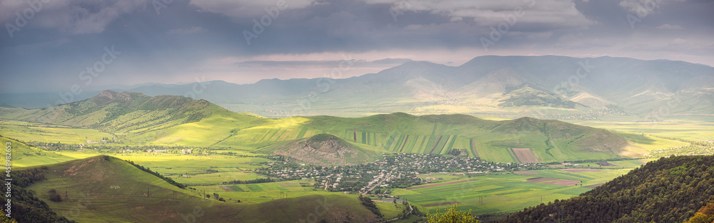 Panoramic view of a distant village in a rural area with a sown agricultural field on a hillside
