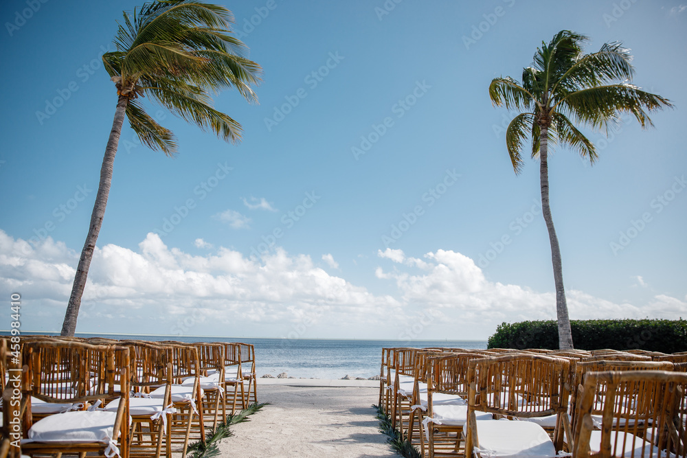Beautiful wooden banquet hall for a wedding reception decoration ready for guests up for an outdoor Beach ocean palm background wedding reception chairs open-air wedding ceremony rows of guest chairs	
