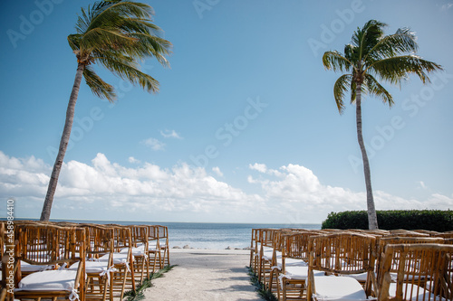Fototapeta Naklejka Na Ścianę i Meble -  Beautiful wooden banquet hall for a wedding reception decoration ready for guests up for an outdoor Beach ocean palm background wedding reception chairs open-air wedding ceremony rows of guest chairs	