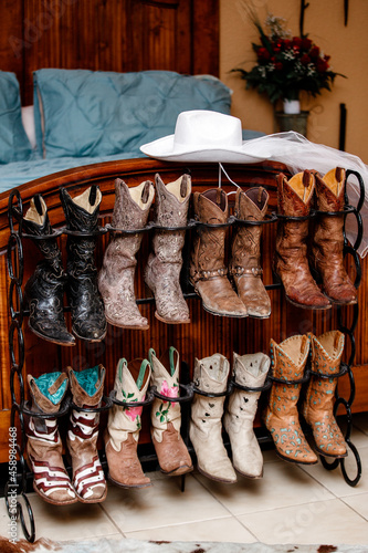 Shoe rack with multicolor Cowboy boots vintage style standing near the wooden bed shoes Colorful cowboy boots Leather West American cowboy boots A western cowboy hat lying upon the shoe rack
