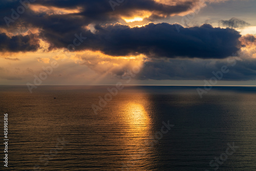 Sunset falls by the sea on a cloudy rainy day, sunlight on the dark surface of the sea © Oleksandr Bochkala