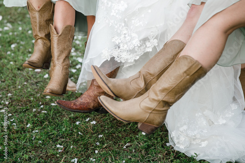 Bride and bridesmaids legs in cowboy boots on the foreground Bride's Wedding Cowboy Boots Details of cowboy boots and shoes Young bride in cowboy boots with her bridesmaids 