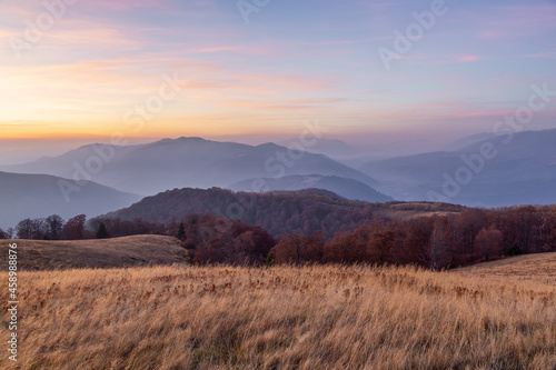 Autumn foggy morning. Landscape with high mountains and orange forest. Panoramic view. Scenery of village. The meadow with yellow grass. Wallpaper background. Touristic place Carpathian park.