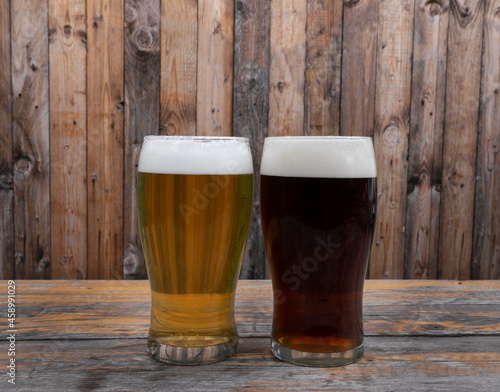 Happy hour. Two glasses of beer, an amber ale and blonde, on the bar wooden table with a wooden background. 