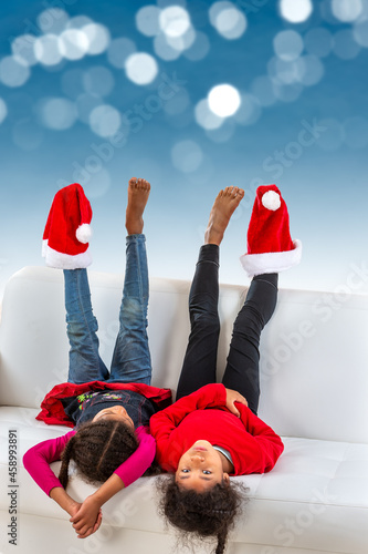 Little girl lying on the sofa on the sofa are having fun with santa claus hat on their feet over a blue bokeh. photo