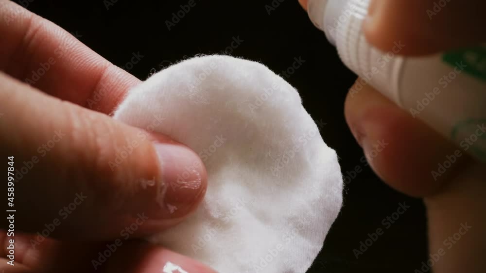 CU, macro: person sprays alcohol antiseptic liquid onto cotton pad to clean germs from surface on black background extreme close view CU, macro: person sprays alcohol antiseptic liquid onto cotton pad to clean germs from surface on black background extreme close view
