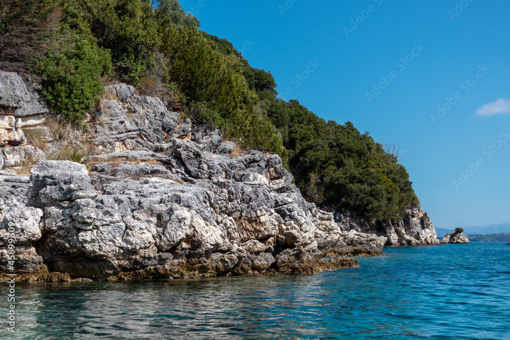 Blue clear Ionian Sea water with scenic green rocky cliffs coast and bright sky. Nature of Lefkada island in Greece. Summer vacation idyllic travel destination