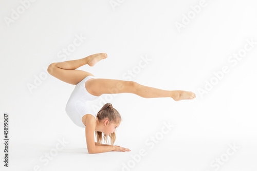 slim artistic teenager girl in white leotard trains on white background in rhythmic gymnastic exercise, children's professional sports photo