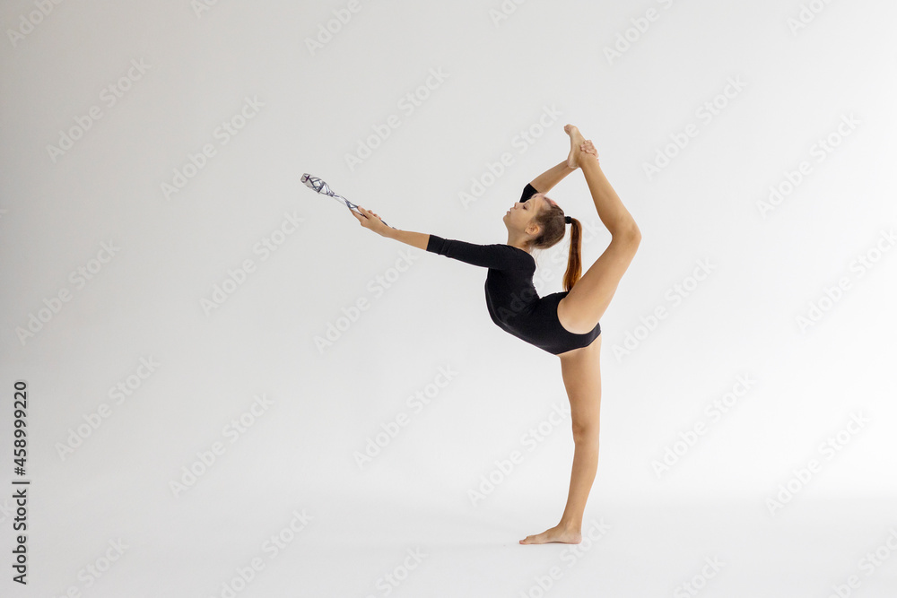 slim artistic teenager girl in black leotard trains on white background with clubs in her hands in rhythmic gymnastic exercise, children's professional sports