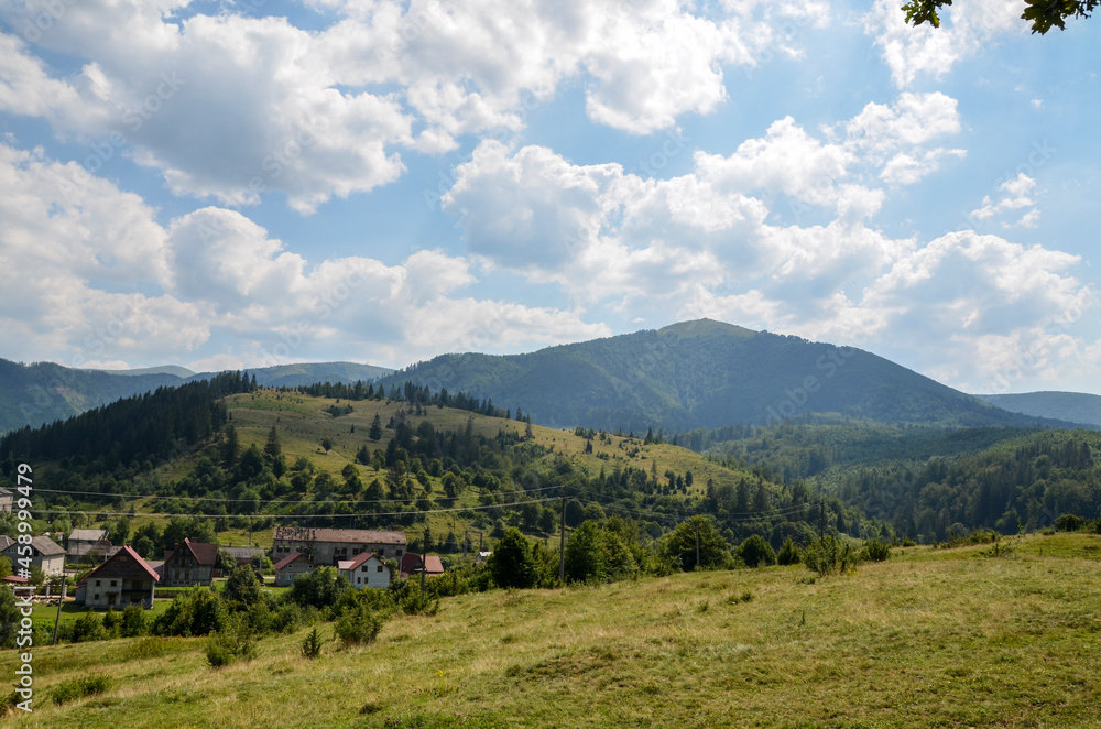Summer landscape of Volovets town in Carpathian mountains. Green fields and hills with houses, Borzhava mountain ridge in a distance. Transcarpathia, Ukraine
