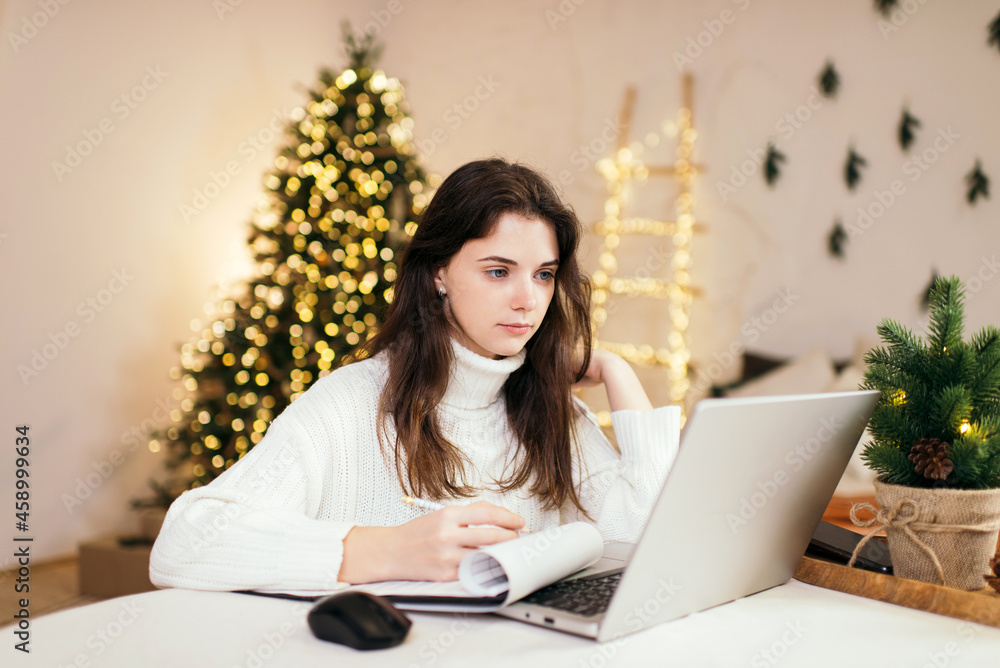 beautiful brunette girl works at home remotely with laptop on the background of a Christmas tree. Quarantine, work on holidays. atmosphere and work at home beautiful brunette girl works at home remotely with laptop on the background of a Christmas tree. Quarantine, work on holidays. atmosphere and work at home