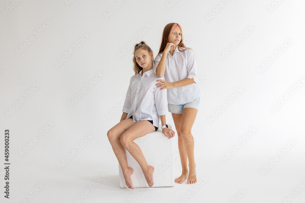 two artistic teenager girls in white shirts and jeans shorts trains and having fun on white background in rhythmic gymnastic exercise, children's professional sports two artistic teenager girls in white shirts and jeans shorts trains and having fun on white background in rhythmic gymnastic exercise, children's professional sports