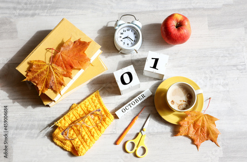 Calendar for October 1 : the name of the month in English, cubes with the numbers 0 and 1, books, alarm clock, maple leaves, red apple, knitted scarf, cup of coffee, eyeglasses on a gray background