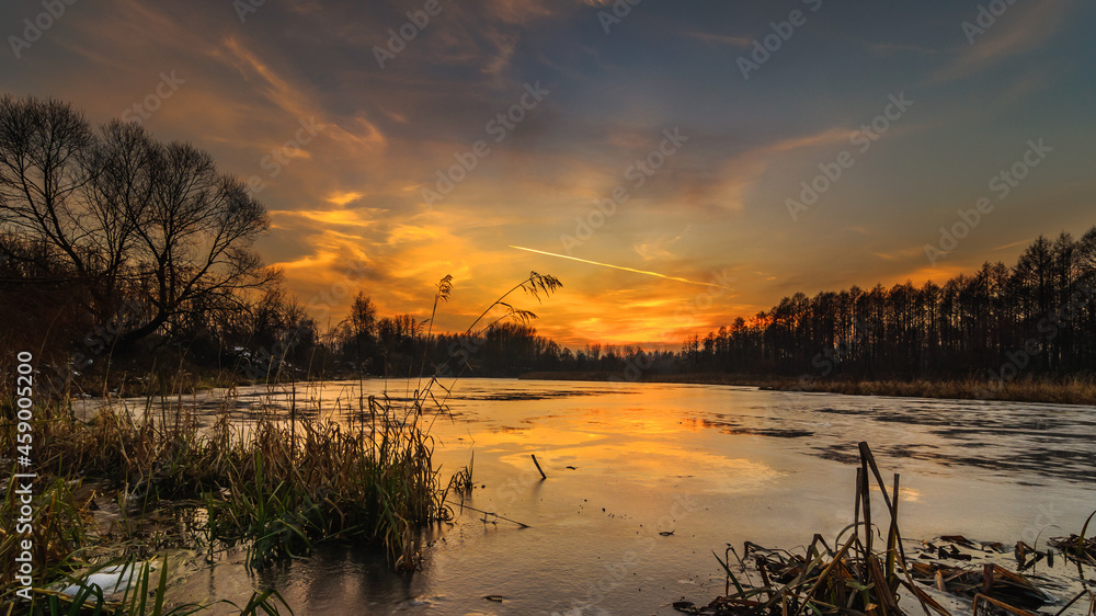 Fototapeta premium winter evening landscape. view of the frozen lake under the dramatic sky after sunset