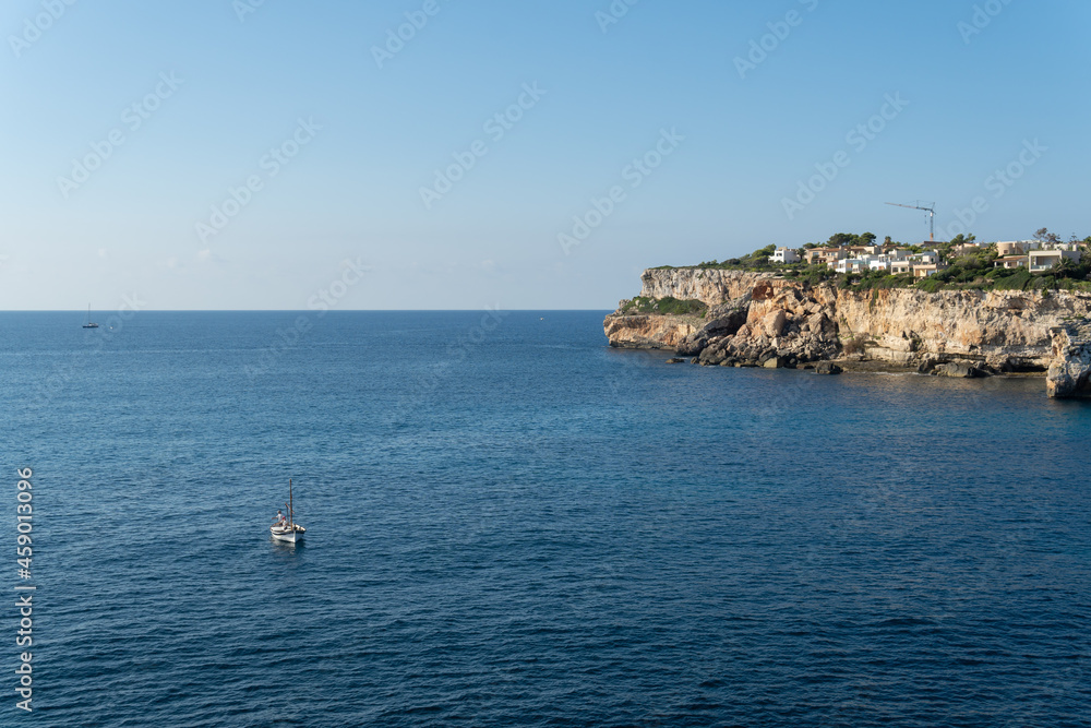 General view of the Mediterranean Sea with a fishing boat, called Llaut, sailing in the sea. Rocky coast of the island of Mallorca, Spain