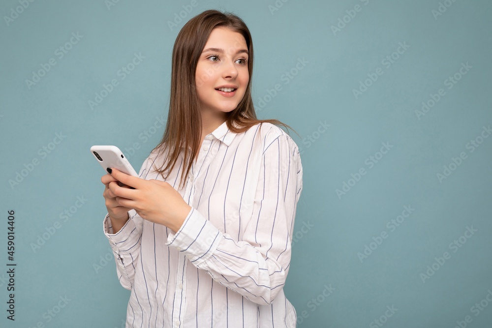 Photo shot of attractive positive good looking young woman wearing casual stylish outfit poising isolated on background with empty space holding in hand and using mobile phone messaging sms looking to Photo shot of attractive positive good looking young woman wearing casual stylish outfit poising isolated on background with empty space holding in hand and using mobile phone messaging sms looking to