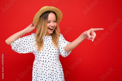 Portrait of beautiful fascinating emotional positive joyful happpy female promoter pointing to the side at copy space for advertising wearing hipster outfit isolated over background wall with empty photo