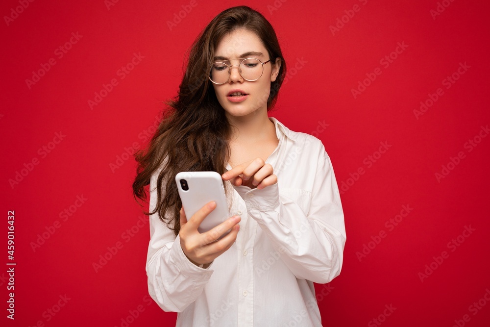 Beautiful young woman wearing casual clothes standing isolated over background surfing on the internet via phone looking at mobile screen Beautiful young woman wearing casual clothes standing isolated over background surfing on the internet via phone looking at mobile screen