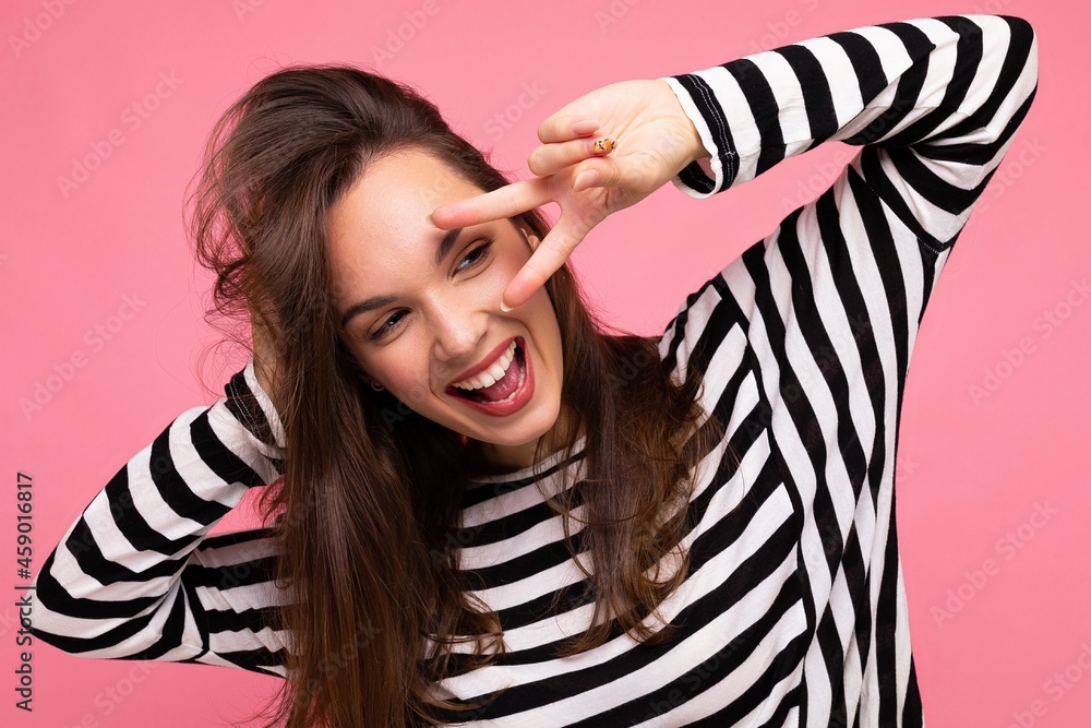 Fototapeta premium Photo of young european positive smiling winsome happy charming brunette woman with sincere emotions wearing casual striped pullover isolated on pink background with copy space