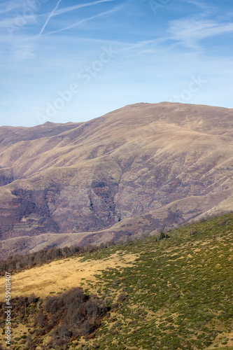 Beautiful wavy highlands covered by dry grass and distant rocky mountain under the blue sky