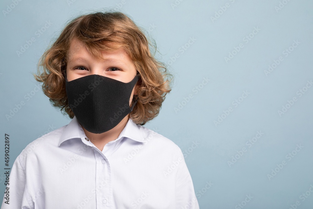 Curly boy wearing an anti virus protection mask to prevent others from corona COVID-19 and SARS cov 2 infection isolated over blue background Curly boy wearing an anti virus protection mask to prevent others from corona COVID-19 and SARS cov 2 infection isolated over blue background
