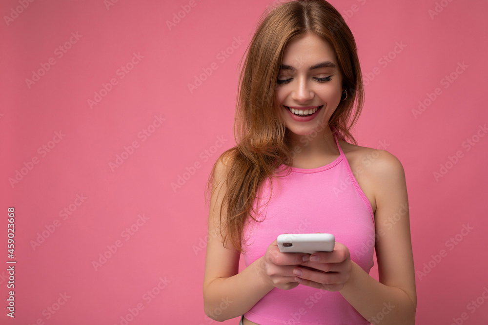 Beautiful smilin happy sexy young woman wearing casual clothes standing isolated over background surfing on the internet via phone looking at mobile screen Beautiful smilin happy sexy young woman wearing casual clothes standing isolated over background surfing on the internet via phone looking at mobile screen
