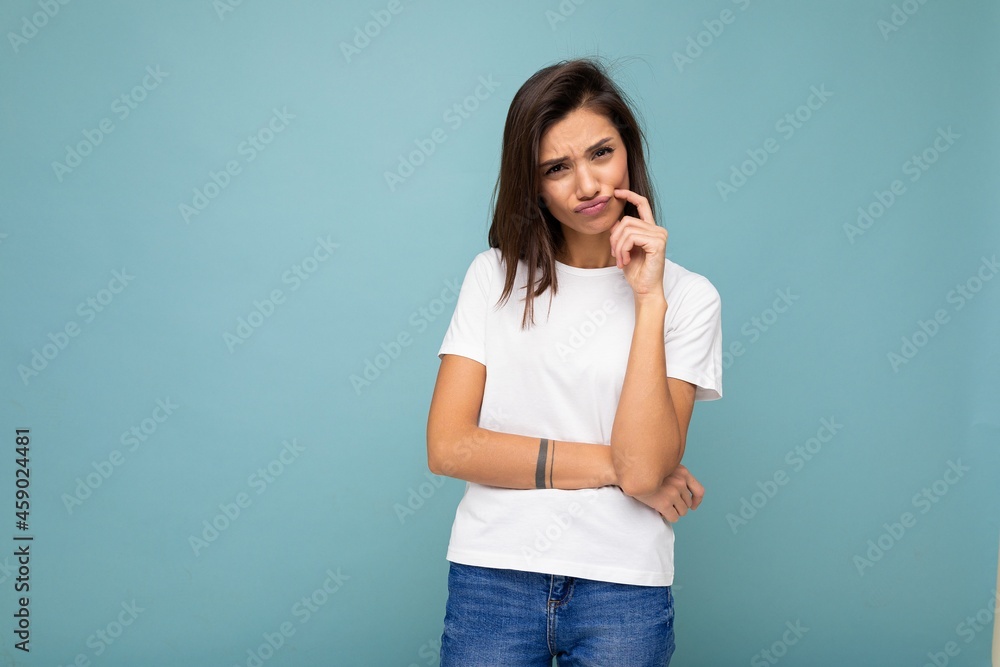 Portrait of sad thinking young pretty nice winsome brunette woman with sincere emotions wearing casual white t-shirt for mockup isolated over blue background with copy space Portrait of sad thinking young pretty nice winsome brunette woman with sincere emotions wearing casual white t-shirt for mockup isolated over blue background with copy space