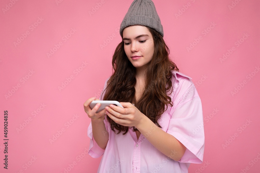 Photo shot of attractive positive good looking young woman wearing casual stylish outfit poising isolated on background with empty space holding in hand and using mobile phone messaging sms looking at Photo shot of attractive positive good looking young woman wearing casual stylish outfit poising isolated on background with empty space holding in hand and using mobile phone messaging sms looking at