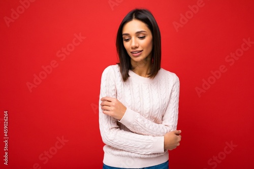 Beautiful cute adorable tender young brunette woman in casual light knitted sweater isolated on red background with free space and enjoying