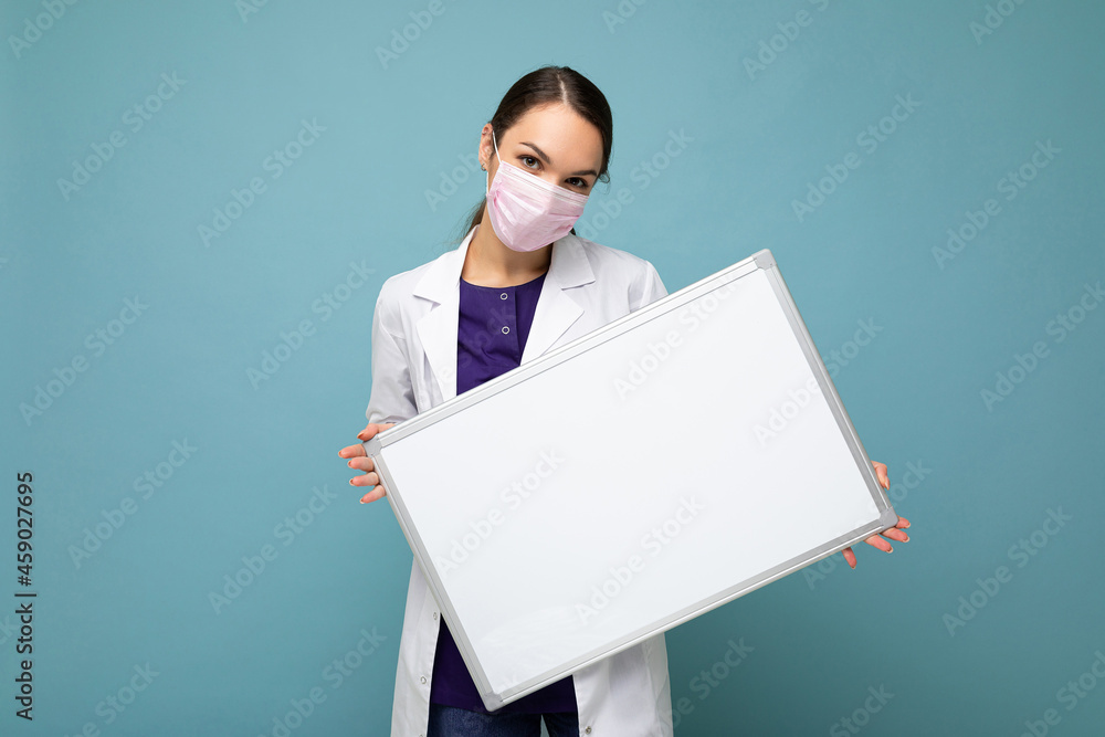 Woman doctor wearing a white medical coat and a mask holding blank board with copy space for text isolated on background. Coronavirus concept Woman doctor wearing a white medical coat and a mask holding blank board with copy space for text isolated on background. Coronavirus concept