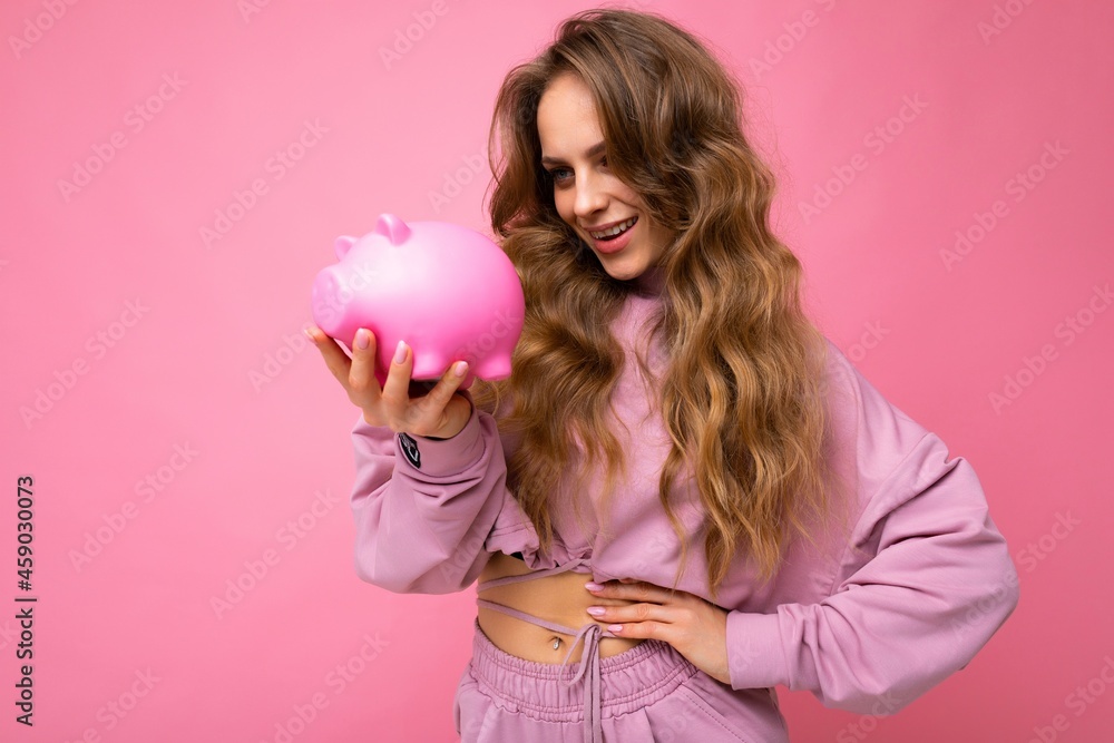 Portrait photo of happy positive smiling young beautiful attractive woman with wavy long blonde hair with sincere emotions wearing stylish pink hoodie isolated over pink background with copy space and Portrait photo of happy positive smiling young beautiful attractive woman with wavy long blonde hair with sincere emotions wearing stylish pink hoodie isolated over pink background with copy space and